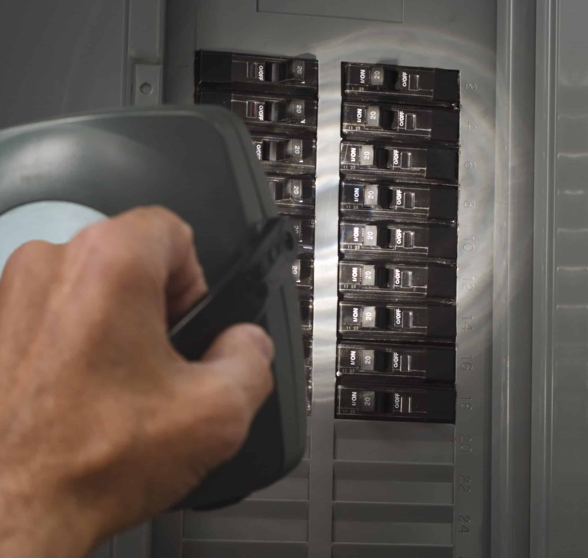 Man examining circuit breakers at residential service panel, transient overvoltage.