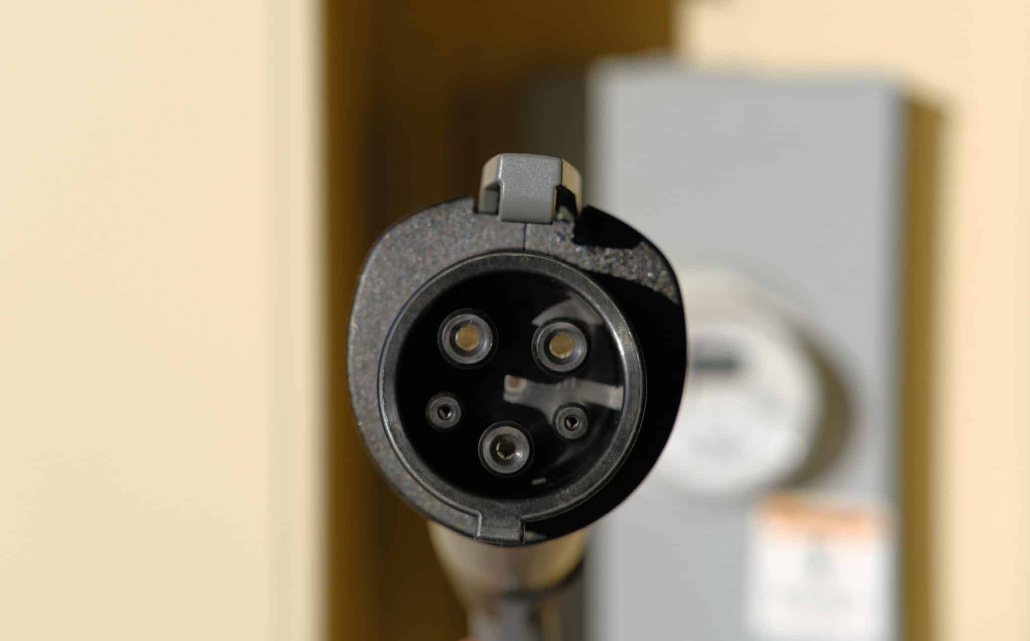 Inspect type 2 EV charging plug with a home electric meter in the background, EV charger maintenance.