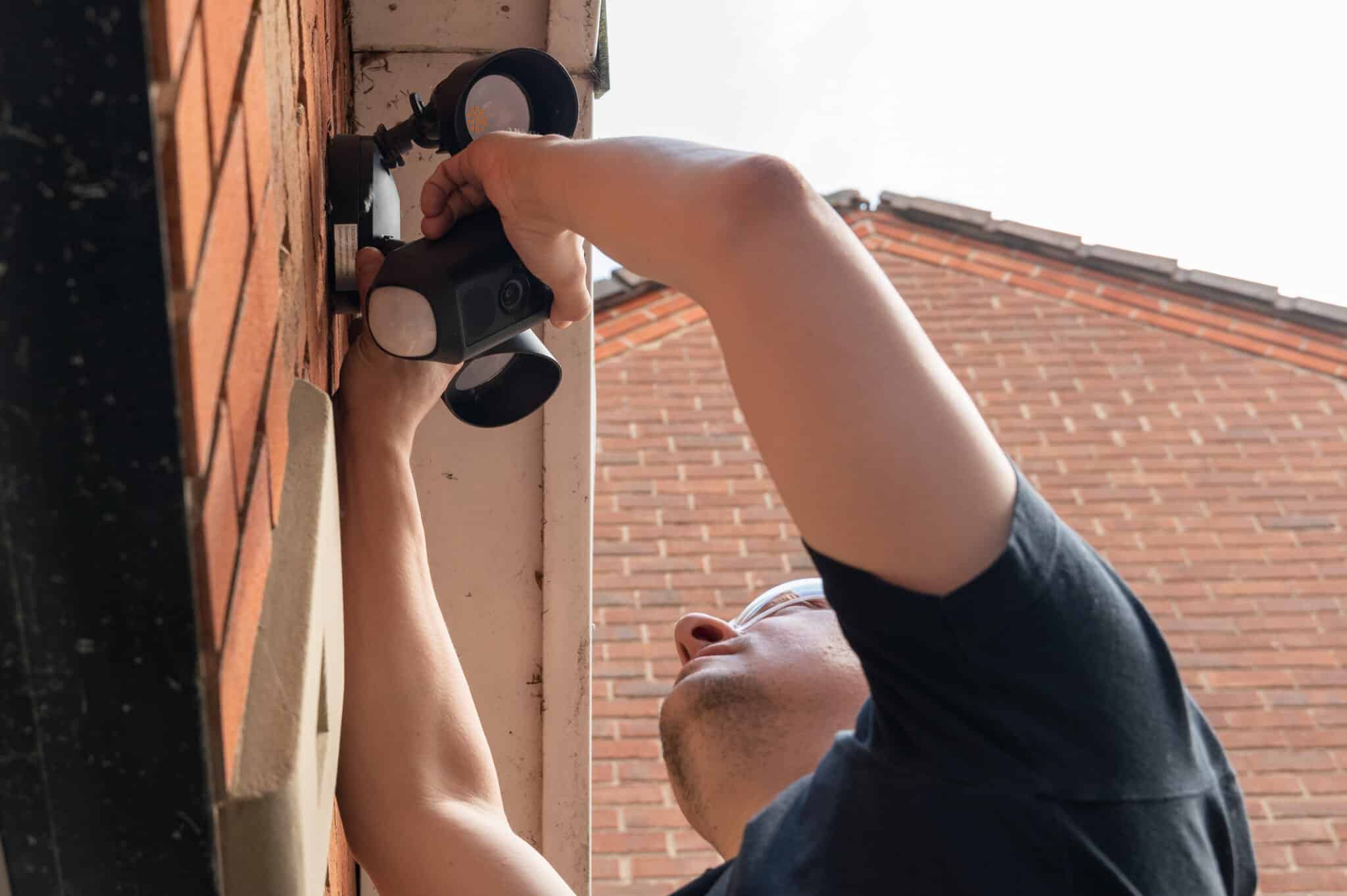 Man installing and adjusting a wireless security camera and spotlights, Motion sensor lights.